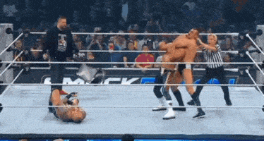 a wrestler is laying on the ground in a wrestling ring while a referee watches