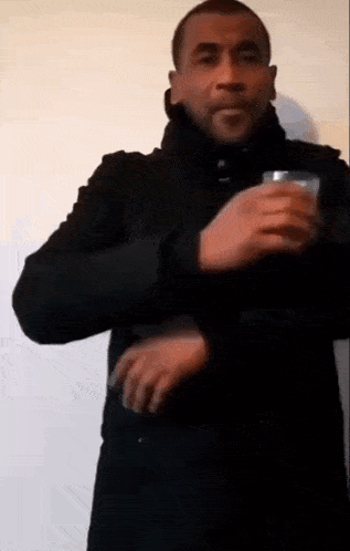 a man in a black coat is holding a glass in his hand and making a funny face .