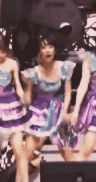 a group of girls in purple and blue dresses are dancing on stage .
