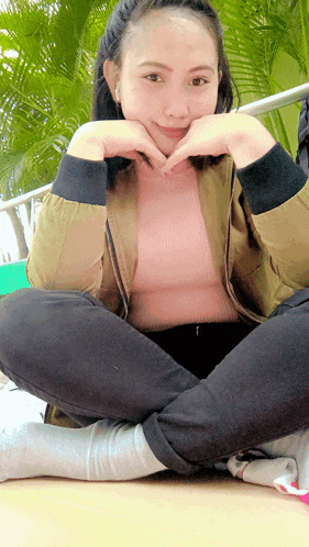 a girl sitting on the floor with her legs crossed and making a heart shape with her hands