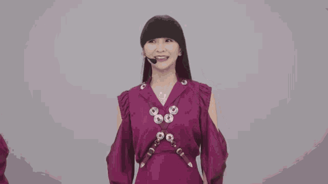 a woman in a purple dress with a microphone on her head is dancing .