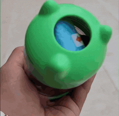 a person is holding a green toy with a blue ball inside