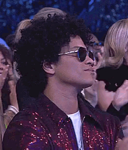 a man wearing sunglasses and a red jacket is clapping in a crowd .