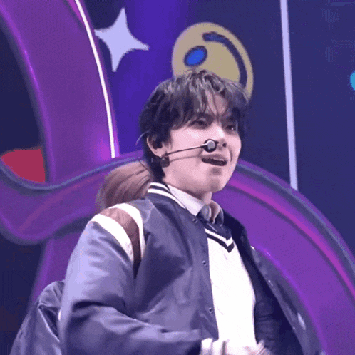 a young man is wearing a microphone and a jacket on a stage .