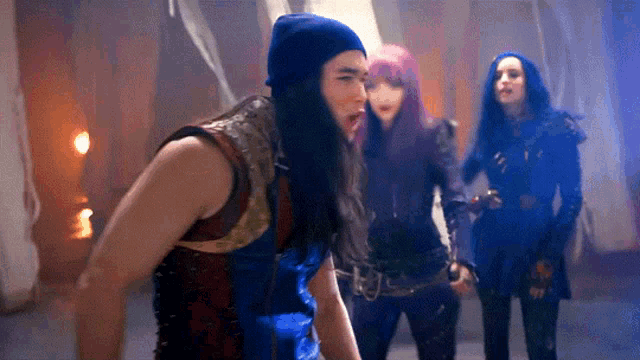a group of girls are standing next to each other in a dark room . one of the girls is wearing a blue beanie .