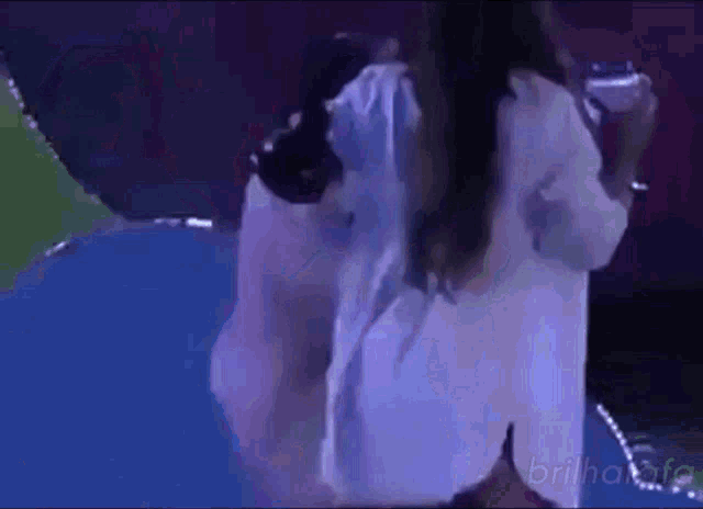 a woman in a white shirt is standing on a blue surface in a dark room .