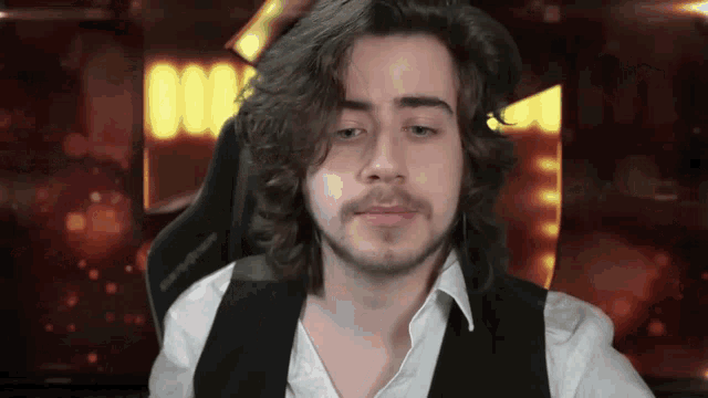 a man with long hair and a beard wearing a black vest