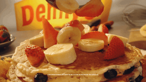 pancakes with bananas strawberries blueberries and syrup on top with a del monte sign in the background