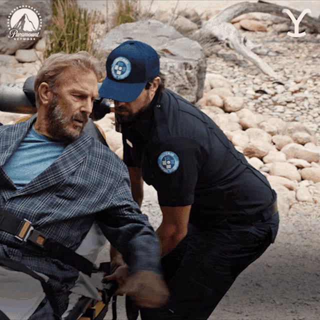a man in a wheelchair is being helped by a paramedic wearing a blue hat with the word rescue on it