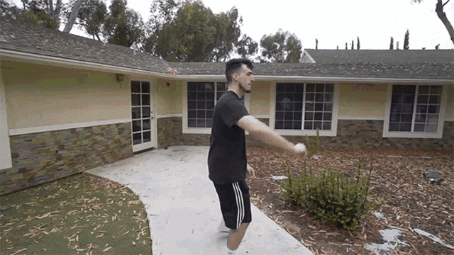 a man in a black t-shirt and black shorts is standing in front of a house