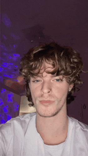 a young man with curly hair is wearing a white shirt and a nose ring