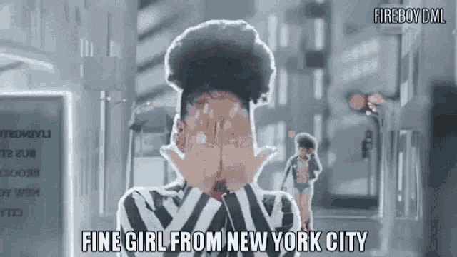 a woman in a striped shirt is covering her face with her hands while standing on a city street .