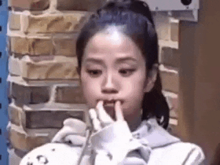 a young girl is holding her finger to her mouth while sitting in front of a brick wall .