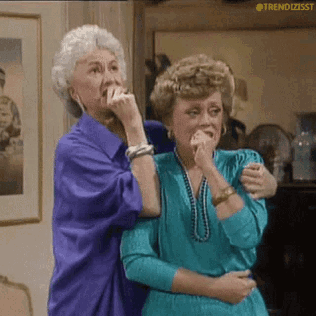 two older women standing next to each other with one covering her mouth with her hand