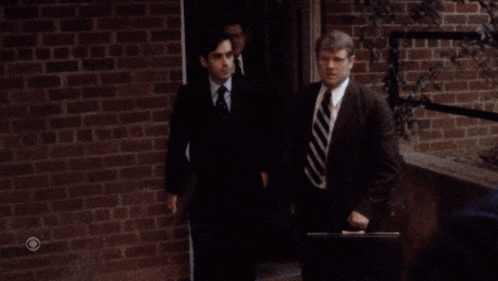 a group of men in suits and ties are walking in front of a brick wall