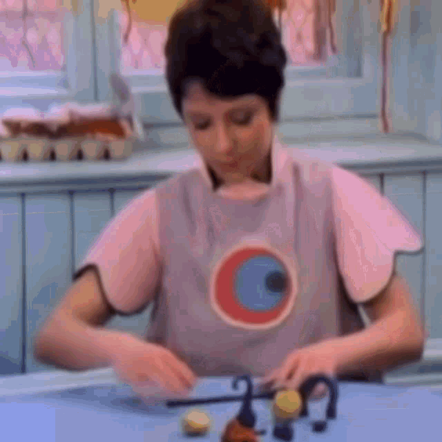 a woman in a pink apron is sitting at a table with a bunch of toys .