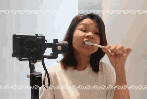 a woman brushing her teeth with a canon camera behind her