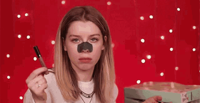 a woman with a nose mask on her face is holding a lipstick .
