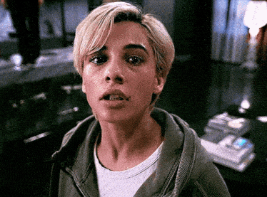 a woman with short blonde hair is wearing a green jacket and a white shirt .