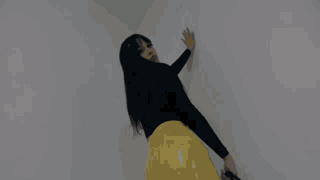 a woman in a black top and a yellow skirt holds a black purse