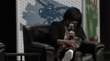 a woman is sitting in a chair holding a microphone and wearing a hood
