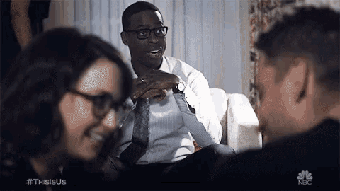 a man in a suit and tie is sitting on a couch talking to a group of people .