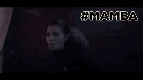 a bald man in a suit is screaming in a dark room with the word mamba behind him .