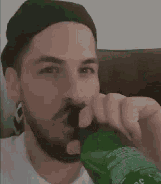 a man with a beard is drinking a green bottle of soda