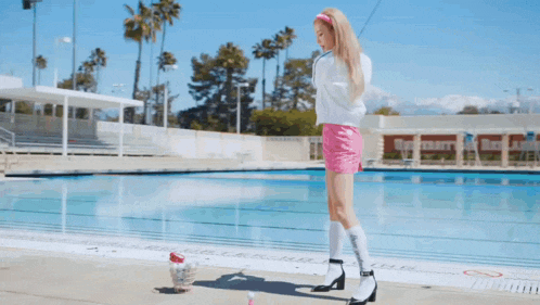 a young woman wearing a white hoodie and a pink headband is standing on a beach looking at the camera .