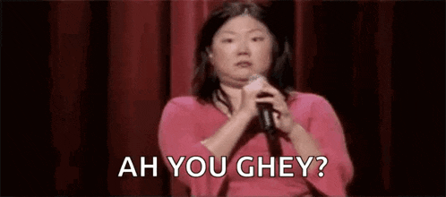 a woman is holding a microphone in front of a red curtain and saying ah you ghey .