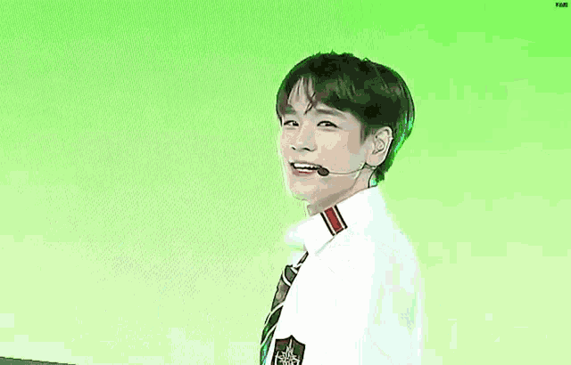 a young man wearing a tie and a microphone is standing in front of a green background .