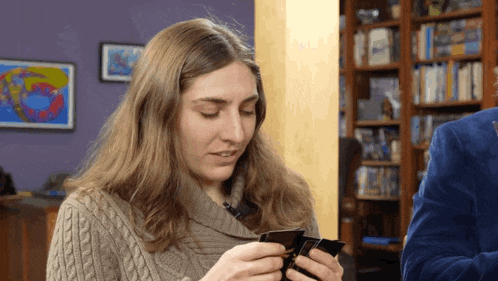 a woman in a sweater is holding a cell phone in her hands