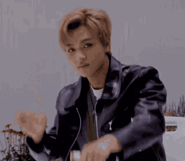 a young man wearing a black leather jacket is waving his hands in the air .