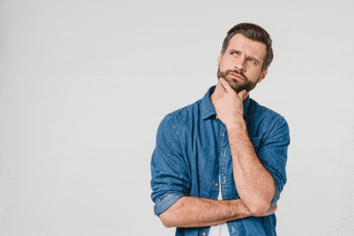 a man in a denim shirt is holding his hand to his chin while looking up .