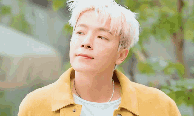 a young man with white hair is wearing a yellow jacket and smiling .
