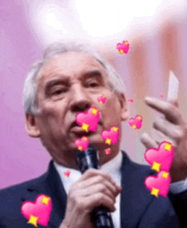 a man in a suit and tie is holding a microphone with pink hearts coming out of his mouth .