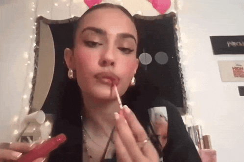 a woman is applying lipstick to her lips in front of a mirror