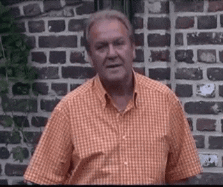 a man wearing an orange plaid shirt stands in front of a brick wall