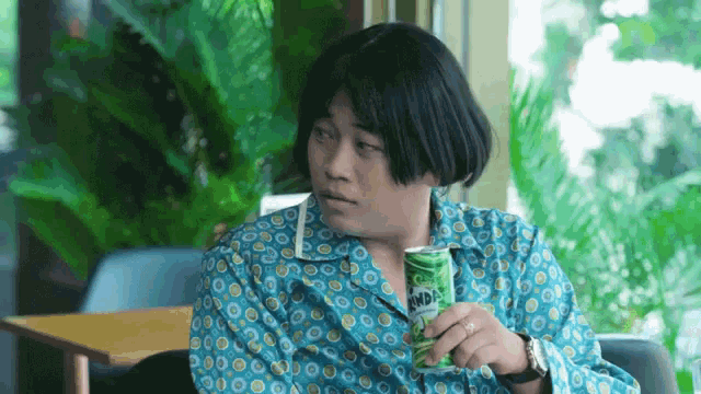 a man wearing a blue shirt is holding a green can of soda