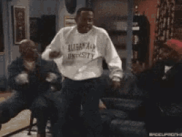 three men are sitting on a couch in a living room and one of them is wearing a sweater that says canadian university