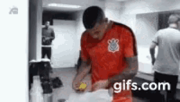 a man in a red shirt is standing in a locker room .