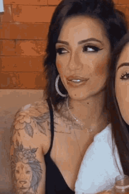 a woman with a tattoo on her shoulder is sitting next to another woman .