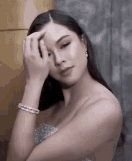a woman in a silver dress is touching her face with her hand .