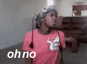 a woman in a pink shirt is standing in a living room with the word oh no written on the bottom .