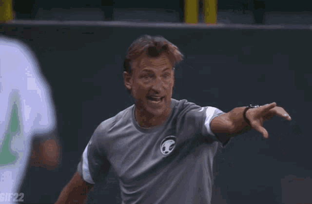 a man wearing a gray shirt with a soccer ball on it is pointing