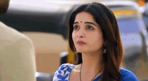 a woman in a blue and white saree is looking at a man in a car .