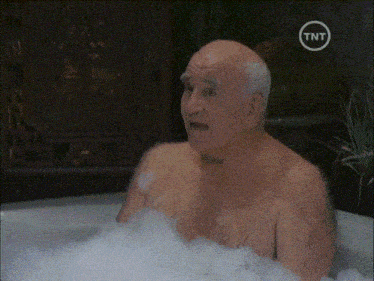 an older bald man is taking a bath in a tub with a tnt logo on the bottom