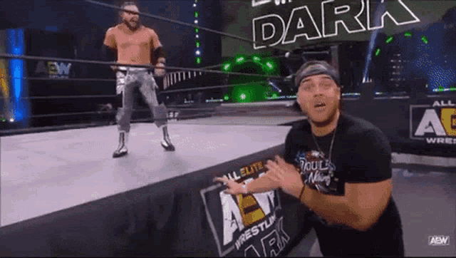 a wrestler is standing in the middle of a wrestling ring while another wrestler stands behind him .