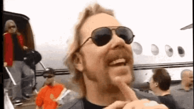 a man wearing sunglasses is smiling while standing in front of an airplane .