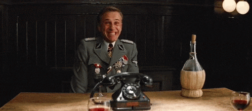 a man in a military uniform is sitting at a table talking on a telephone and smiling .